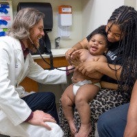Dr. Jason Yaun checking up on toddler in diaper being held by their mother in ULPS Clinic